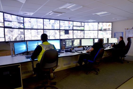 Security control room with multiple operators monitoring a wall of CCTV camera feeds and desktop screens, used for logistics and Workplace surveillance system